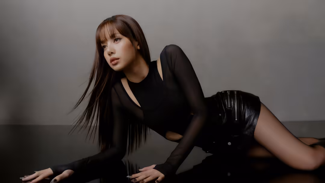 Woman with long dark hair and bangs wearing black outfit posed against neutral gray background in dramatic studio lighting
