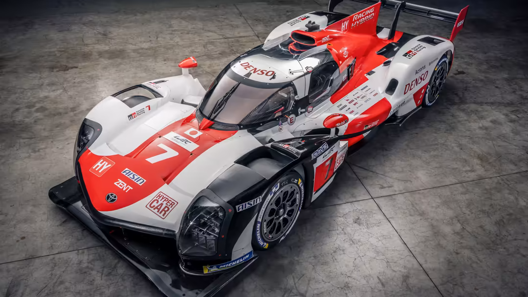 Red and white Toyota GR010 Hybrid hypercar race car photographed from above on concrete surface