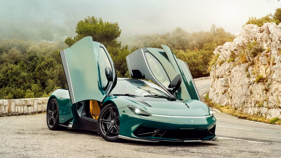 Green Pininfarina Battista hypercar with gull-wing doors open on mountain road, limestone cliffs and forested landscape in ba