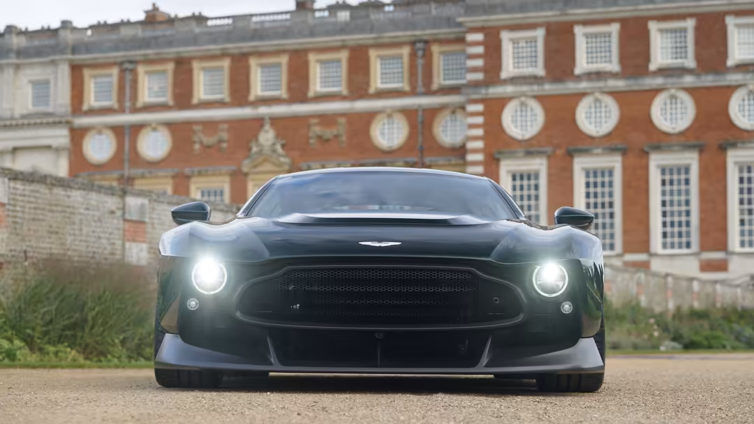 Black Aston Martin Victor supercar with headlights on, parked in front of historic red brick palace building
