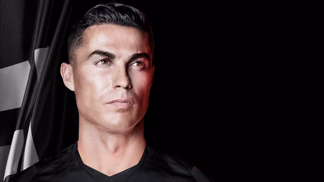 portrait of a person in a black v-neck shirt against a dark background with dramatic red and white lighting from the left.