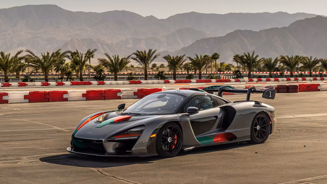 McLaren Senna supercar with tricolor livery parked on desert race track with mountains and palm trees in background