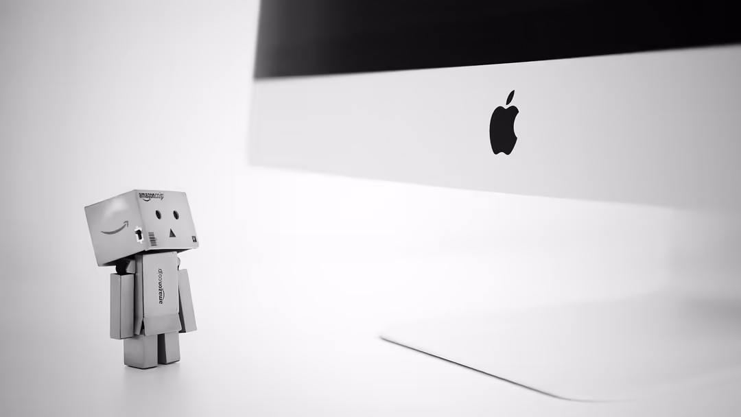 Minimalist office setup with cardboard robot figurine and Apple iMac on white desk in black and white