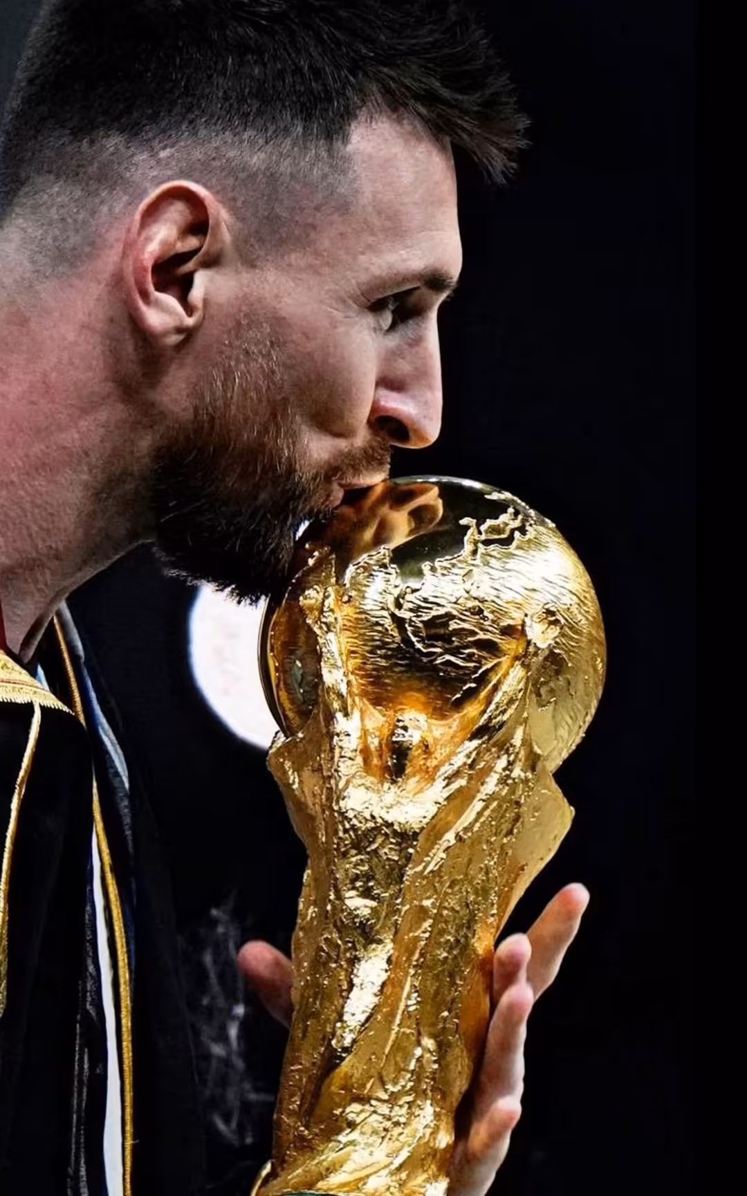 Athlete in dark jersey holds gleaming golden FIFA World Cup trophy against black background, capturing triumphant championshi