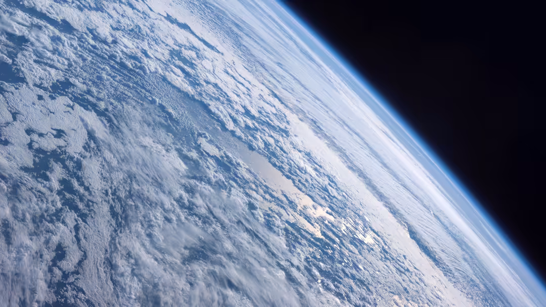 Earth's curved horizon with white clouds and blue atmosphere viewed from space against the darkness of the cosmos