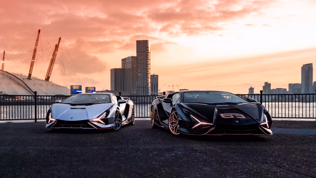 Two sleek Lamborghini Sián FKP 37 supercars parked on waterfront promenade at sunset with city skyline and iconic architectur