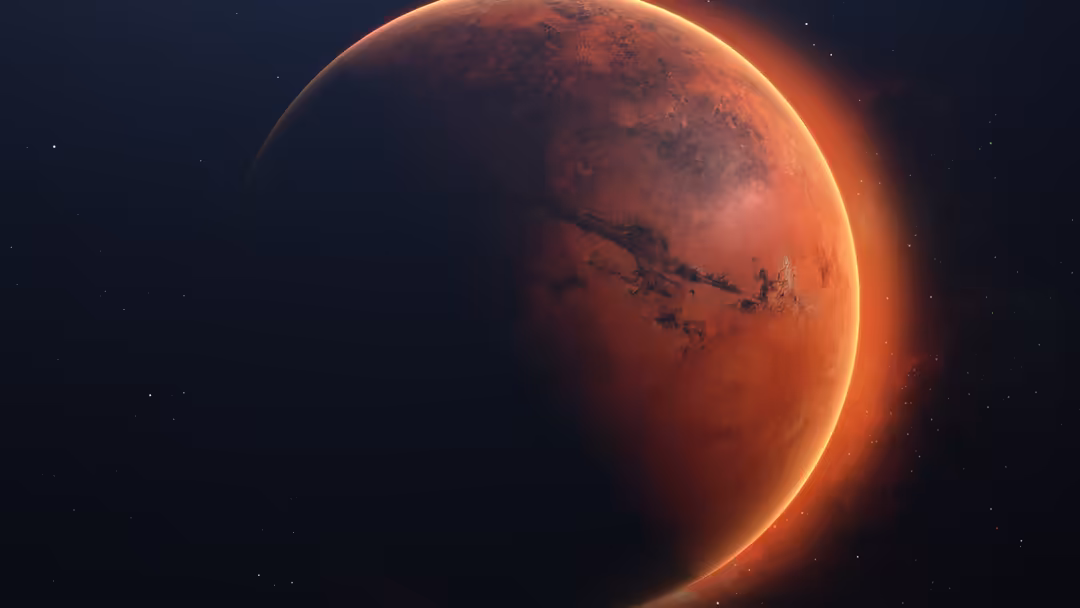 Red planet Mars illuminated by golden sunlight against dark starry space, showing surface details and atmospheric glow around