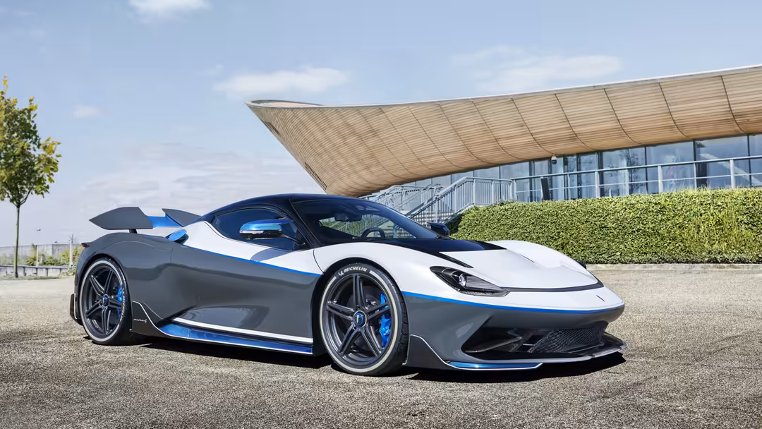 Sleek white and blue Pininfarina Battista Anniversario hypercar parked in front of modern architecture with green hedges