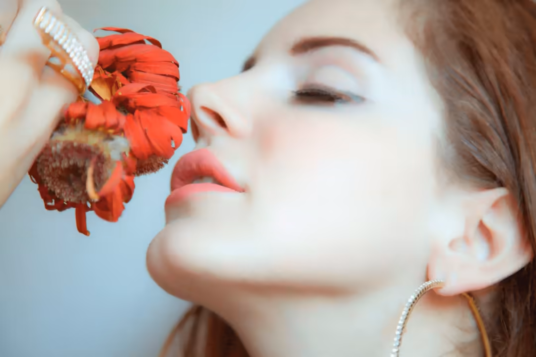 Portrait of woman with closed eyes holding wilted red flower against light blue background, serene aesthetic