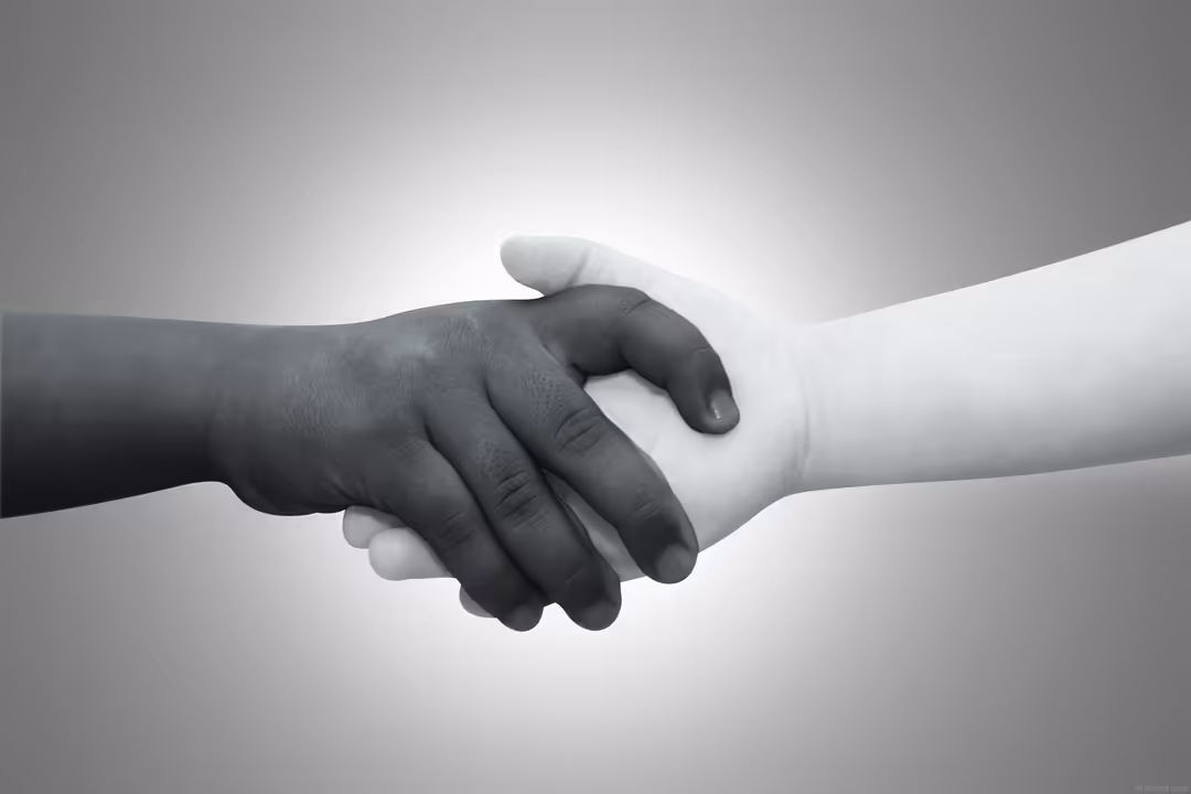 Two hands clasping together in a handshake, one with darker skin and one with lighter skin, symbolizing friendship, unity, an
