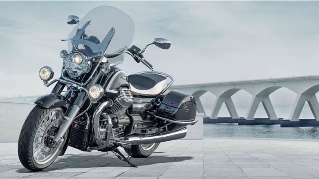 Classic motorcycle with chrome details and windscreen parked on waterfront promenade, elegant bridge arches visible across ca