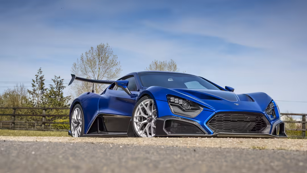 Striking blue Zenvo TSR-S hypercar displayed on rural road with open door, featuring aerodynamic design and white alloy wheel