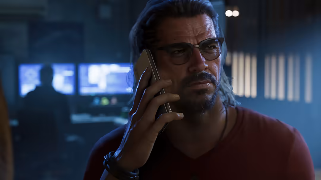 Man in glasses talking on phone in dimly lit room with blue neon lighting and digital displays in background