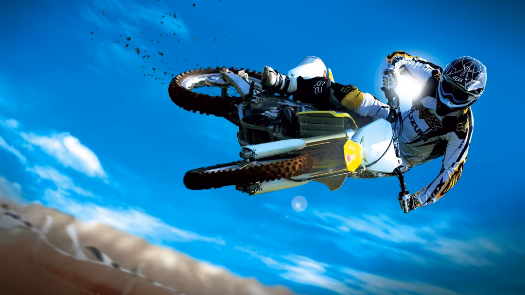 Motocross rider performing aerial stunt on dirt bike against clear blue sky with yellow and white gear visible