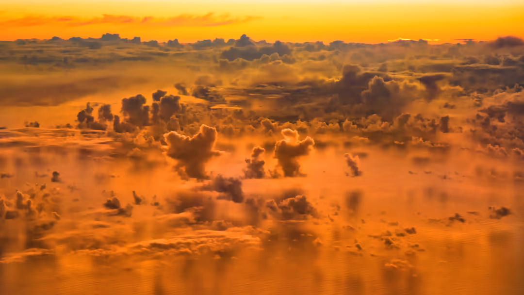 Aerial view of billowing golden clouds illuminated by warm sunrise light, creating a dramatic textured landscape above the ho