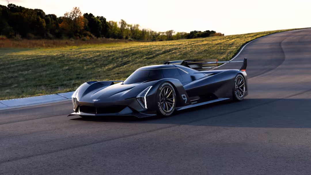 Sleek black Cadillac Project GTP hypercar on curved asphalt road with green fields and trees in background