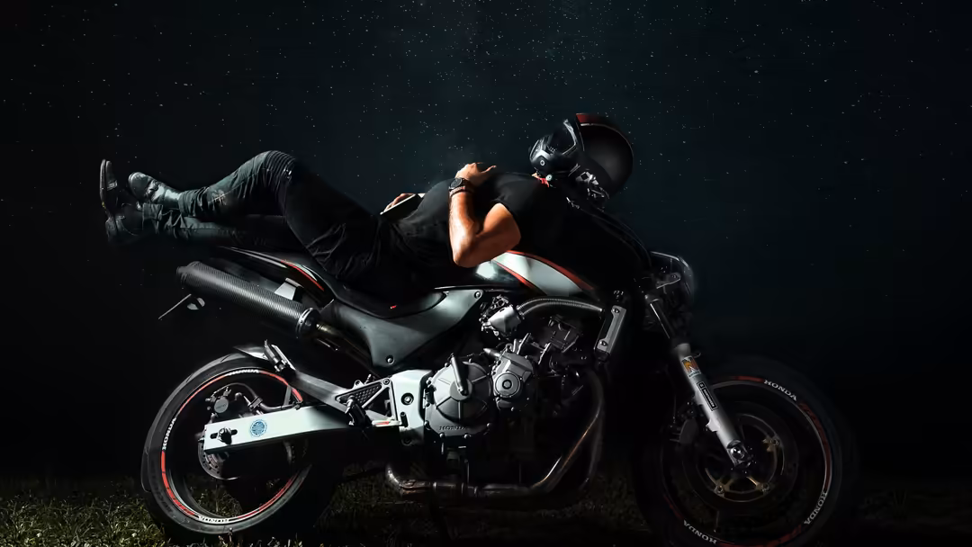 Skilled rider performing dramatic stunt on motorcycle at night, wheelie with one leg extended, dark atmospheric background