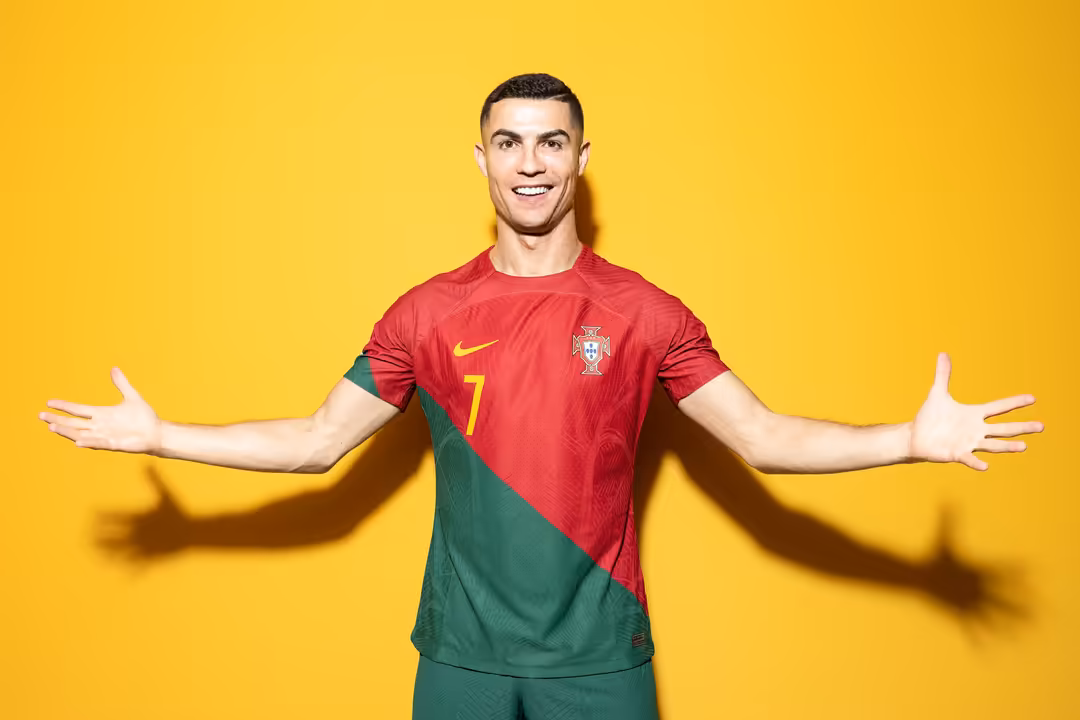 Cristiano Ronaldo wearing Portugal national team red and green jersey with number 7, smiling with arms outstretched against b