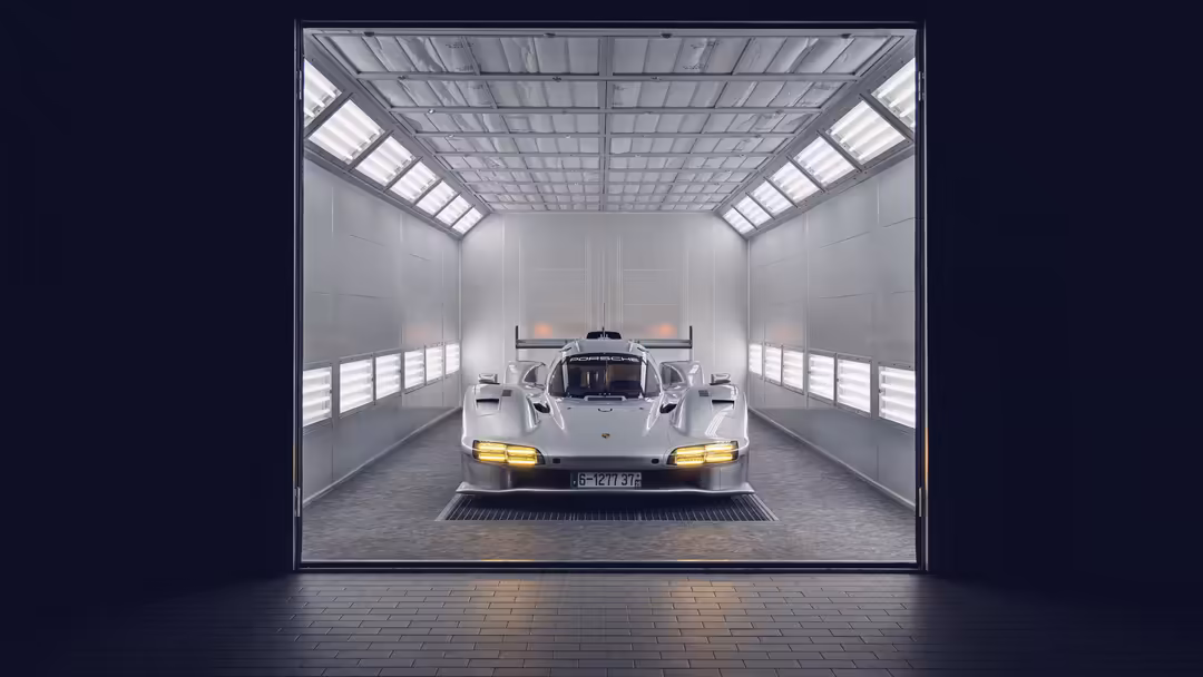 White Porsche 963 RSP supercar parked in modern minimalist garage with bright overhead lights and yellow headlights illuminat