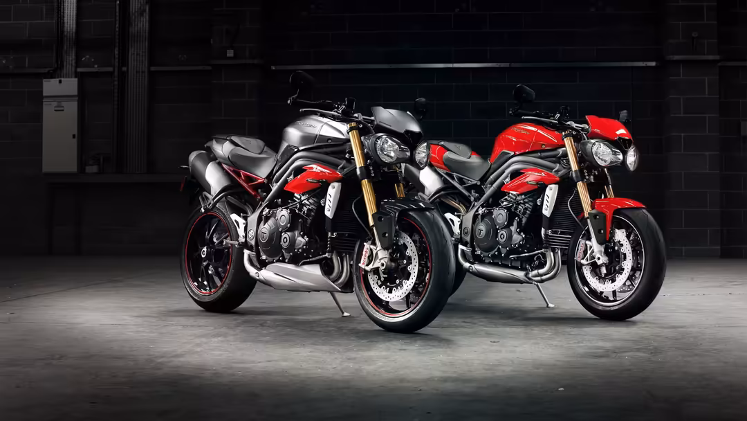 Three powerful motorcycles with red and silver finishes lined up in a dark industrial garage, showcasing detailed engineering