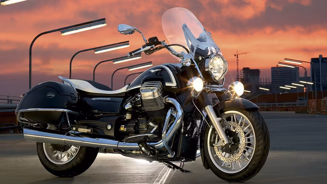 Black cruiser motorcycle with chrome details and sidecar parked on urban rooftop at sunset with dramatic orange sky and city