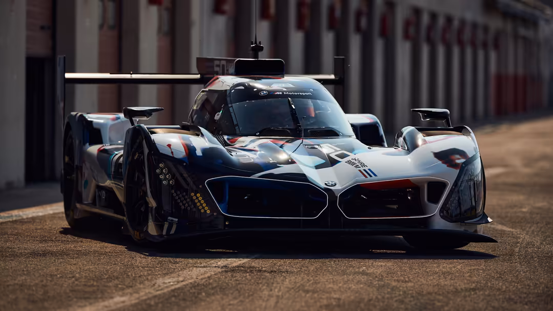 White and black BMW M Hybrid V8 race car with aerodynamic wing on circuit track, high-performance motorsport vehicle