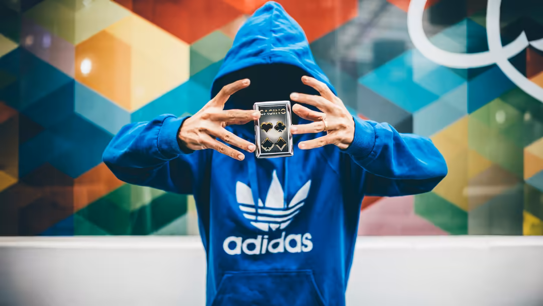 Person in blue Adidas hoodie holding tarot cards against colorful geometric graffiti wall backdrop