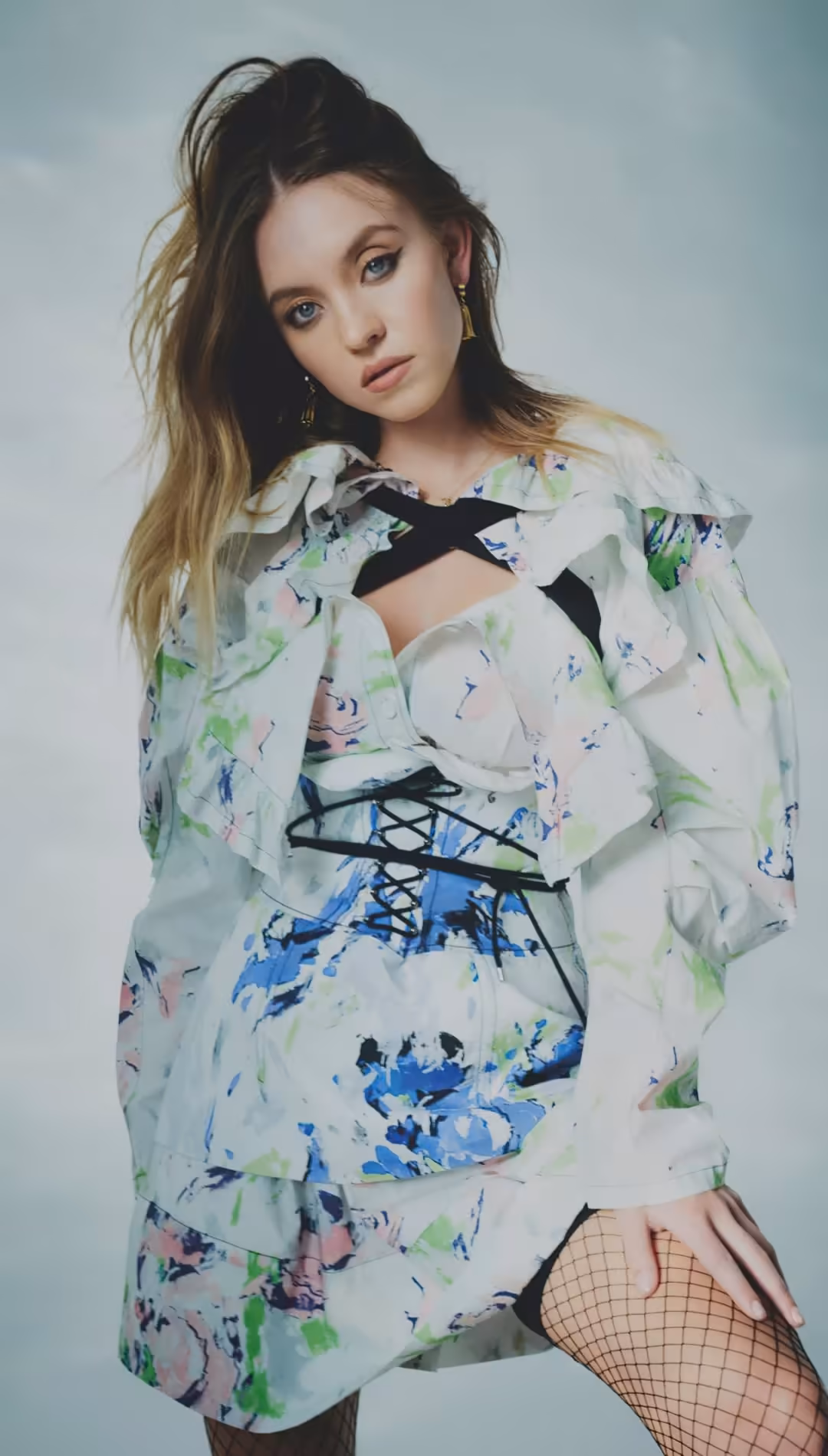 Sydney Sweeney wearing a colorful floral jacket with blue and green botanical patterns over a black crop top against a soft b