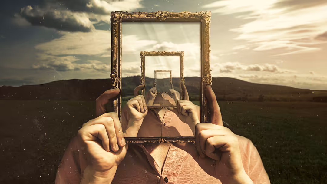 Hands holding nested golden ornate frames showing infinite perspective overlooking expansive green field and cloudy sky