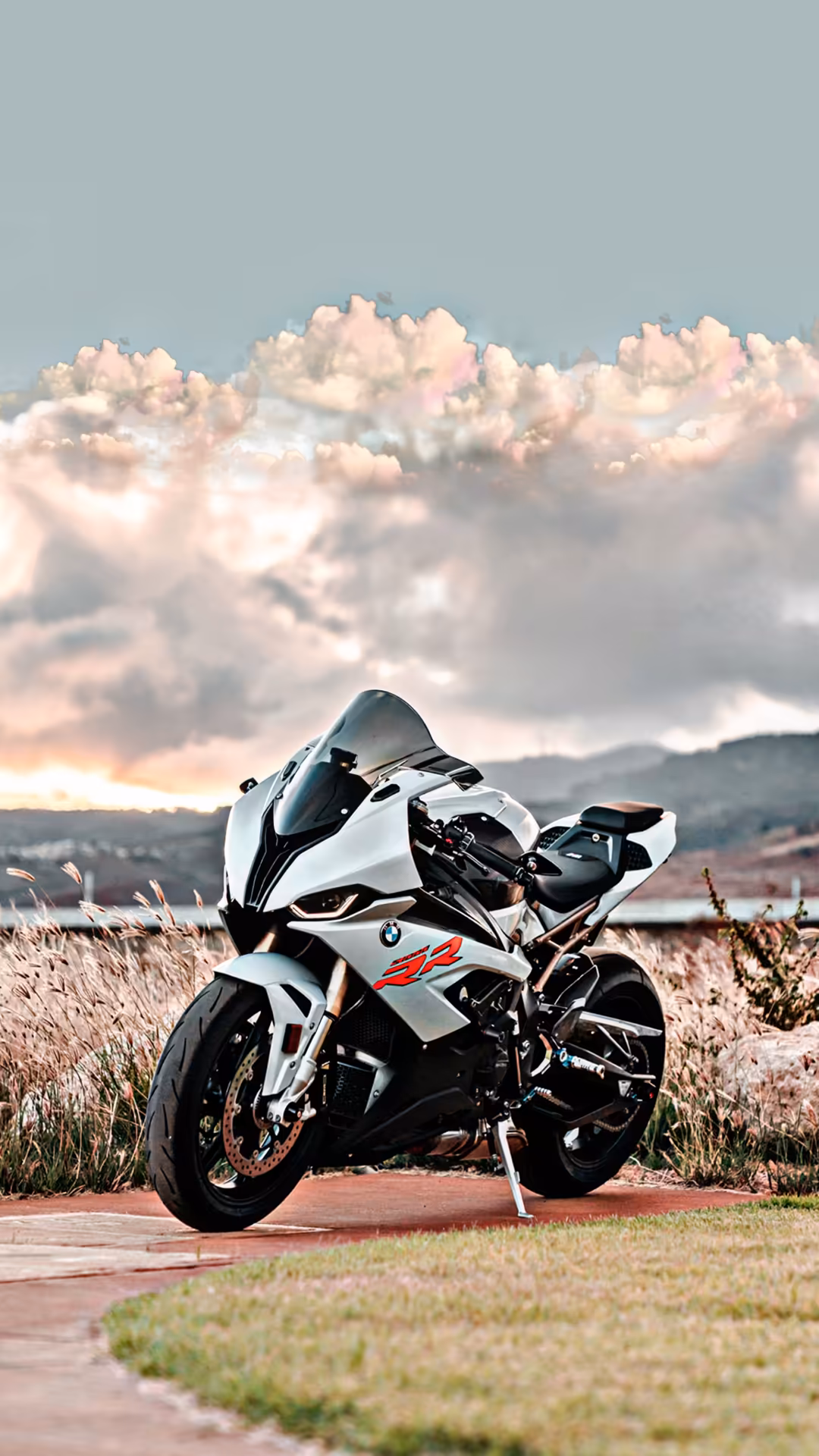 White and black sport motorcycle parked on brick pavement with dramatic pink-tinted clouds and mountain landscape in backgrou