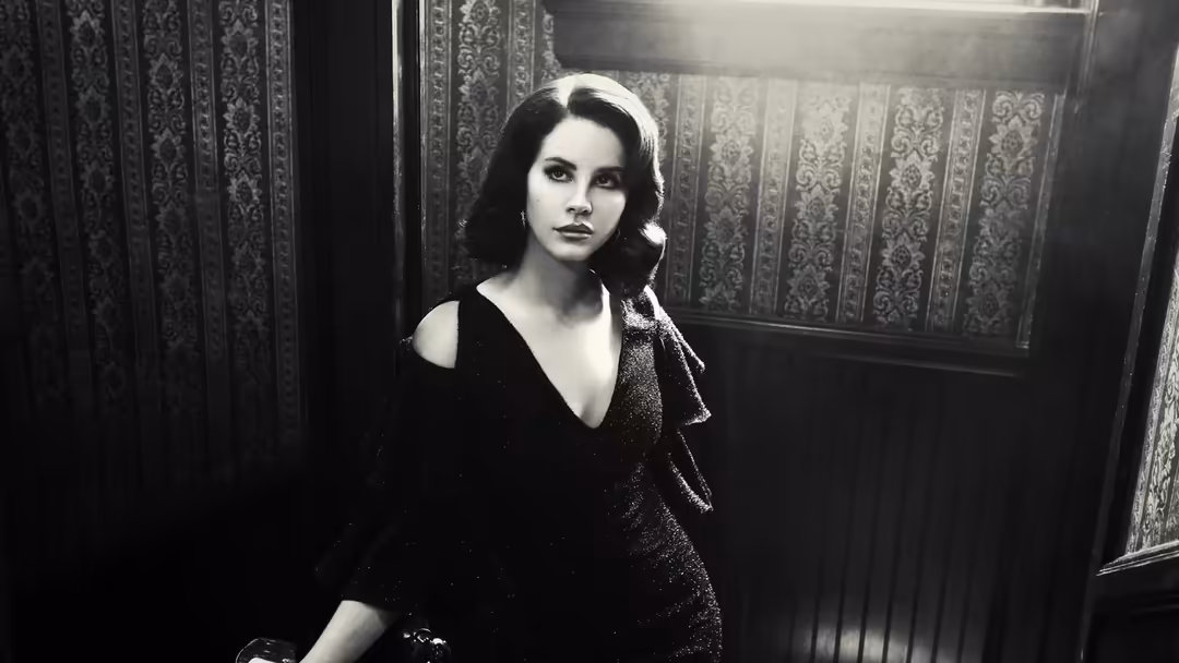 Black and white vintage-style portrait of Lana Del Rey wearing dark clothing against ornate damask wallpaper, classic Hollywo