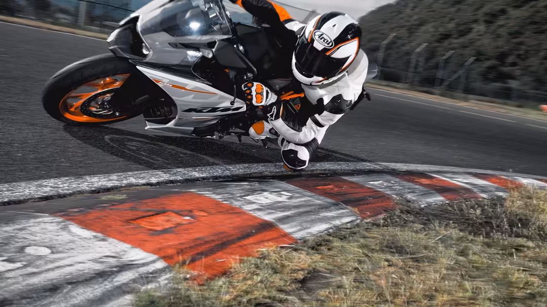 Sport motorcycle leaning aggressively through a race track corner with rider in white helmet and gear, orange and white bike