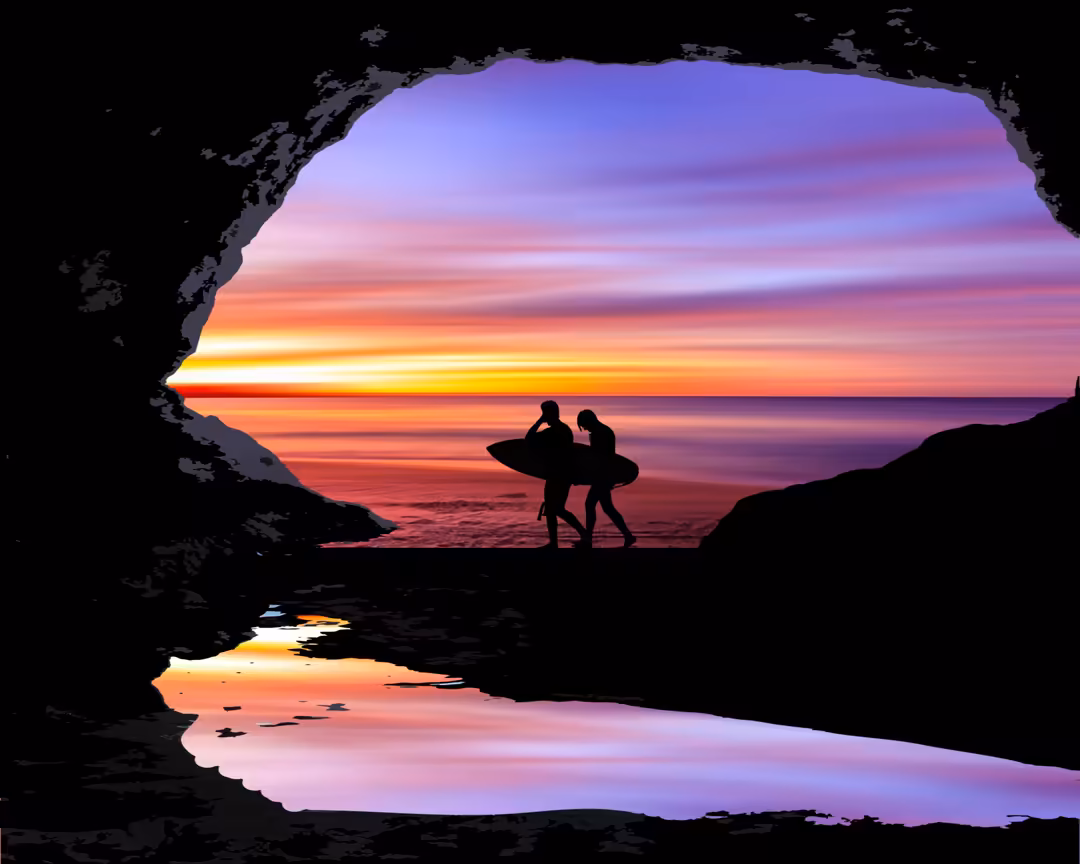Two surfers with boards silhouetted in a cave opening, gazing at a vibrant sunset over the ocean with purple and orange skies