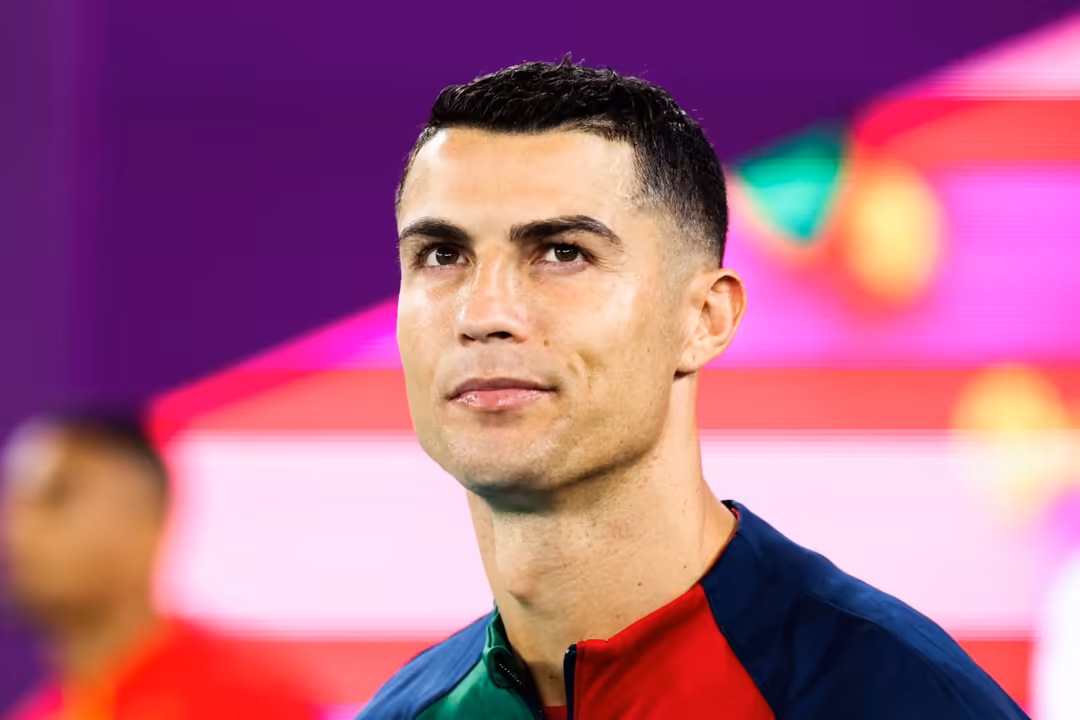 Cristiano Ronaldo wearing red and blue Portugal jersey against vibrant neon pink and purple blurred lights background