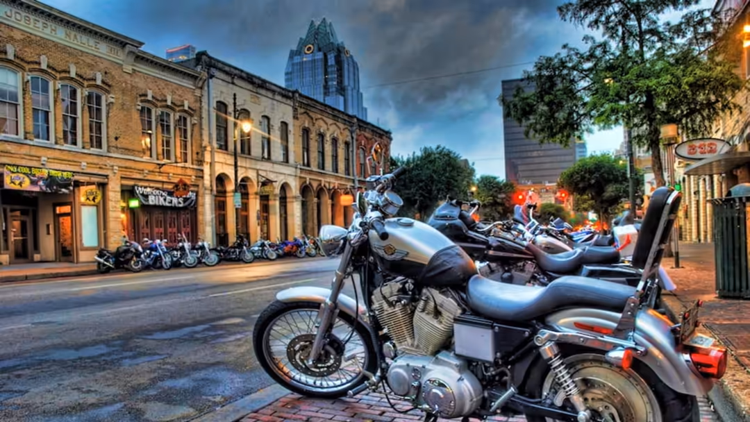 Classic motorcycles lined up on brick street with historic buildings and modern skyscraper backdrop in urban downtown setting