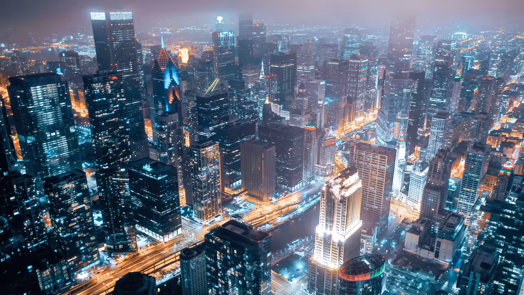 New York City skyline at night with glowing blue and orange neon lights illuminating towering skyscrapers and bustling urban