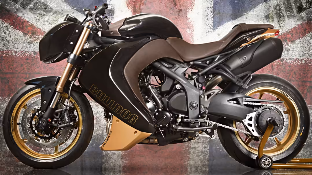 Black and gold custom streetfighter motorcycle with aggressive styling, golden wheels, and brown leather seat against distres