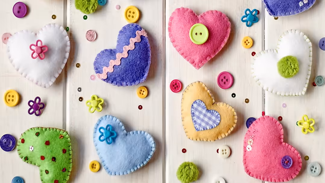 Colorful felt hearts with decorative buttons and flower embellishments arranged on white wooden planks background