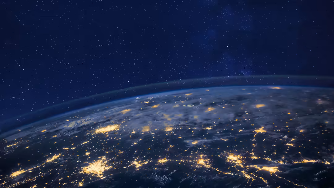 Earth viewed from space at night, showing city lights and glowing continents against a starry sky and dark atmosphere