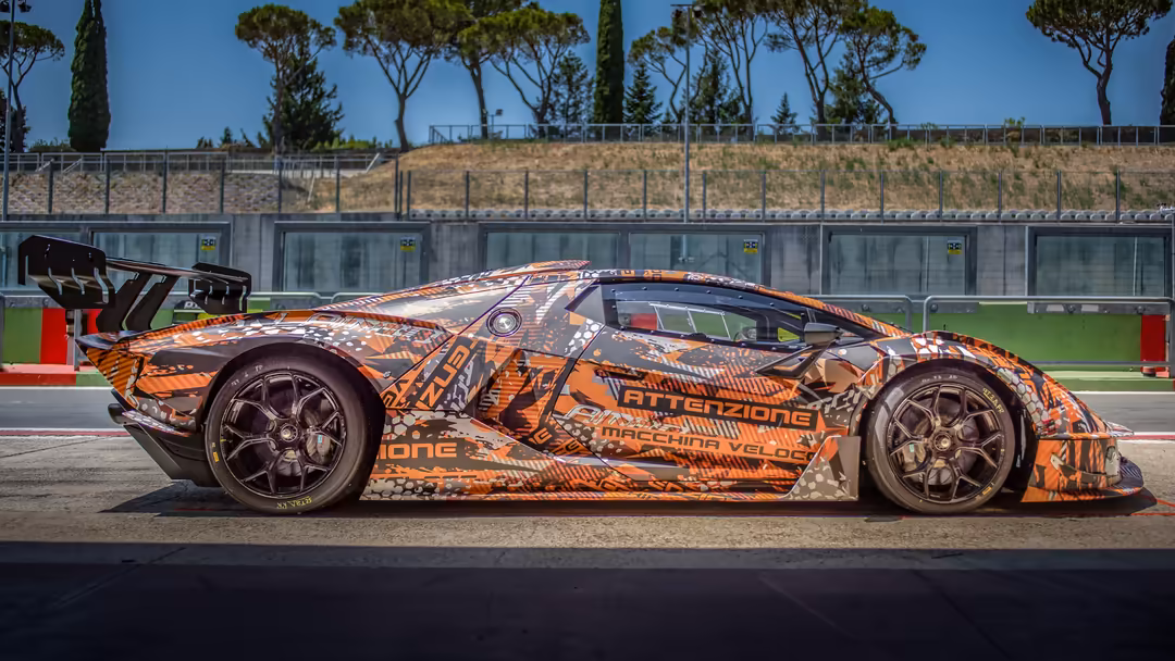 Orange and black Lamborghini Essenza SCV12 supercar on racing circuit track with modern grandstand facilities in background