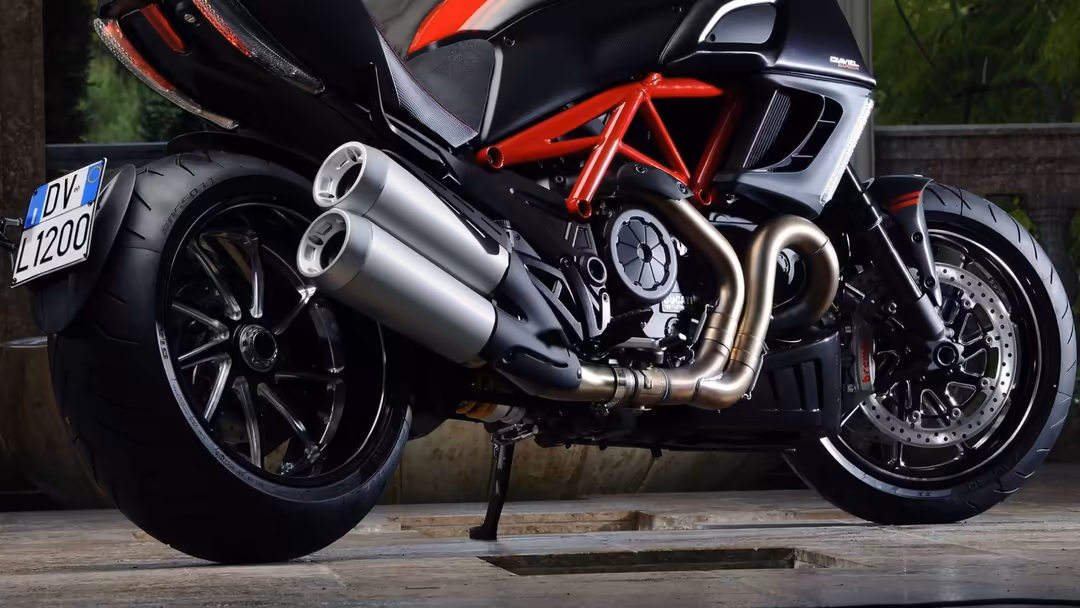 Sleek sport motorcycle with striking red trellis frame, polished chrome dual exhaust pipes, and black fairings parked on conc
