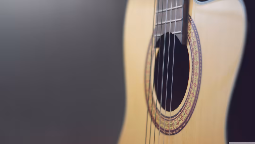 Close-up of a classical acoustic guitar with ornate rosette detailing, nylon strings, and warm natural lighting against a neu