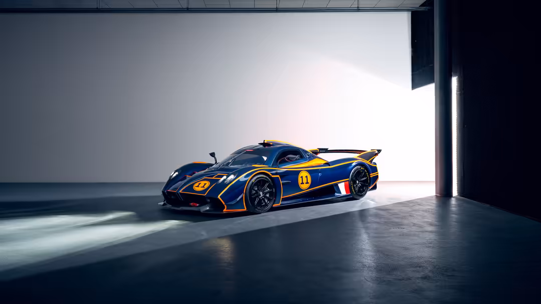 Blue and gold Pagani Huayra R hypercar with racing number 11 displayed in minimalist garage with dramatic natural lighting