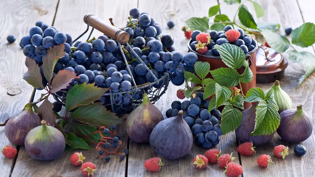 Abundant fresh blueberries and raspberries with dark figs arranged on weathered white wooden surface with green leaves and vi