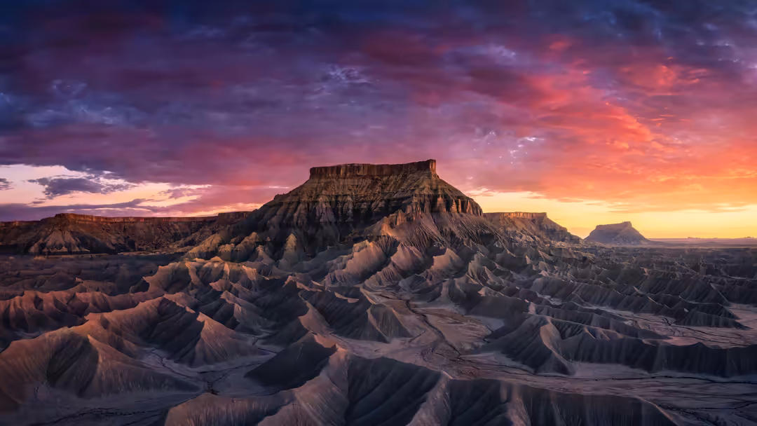 Dramatic desert mountain landscape with golden sunset sky featuring purple and orange hues illuminating layered rock formatio
