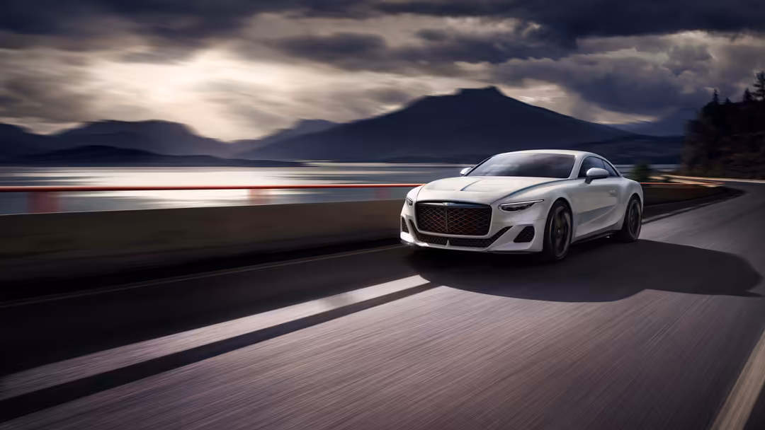 White Bentley Mulliner Batur luxury sports car driving along a scenic lakeside road with dramatic mountains and cloudy sky in