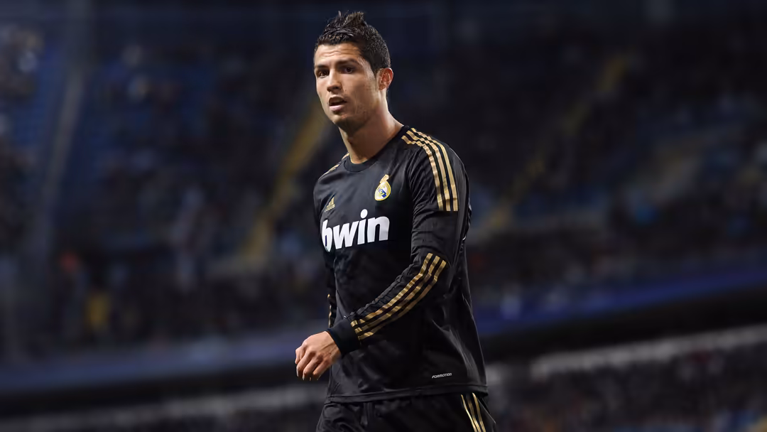Professional footballer wearing black and gold kit during stadium match, focused expression while in play