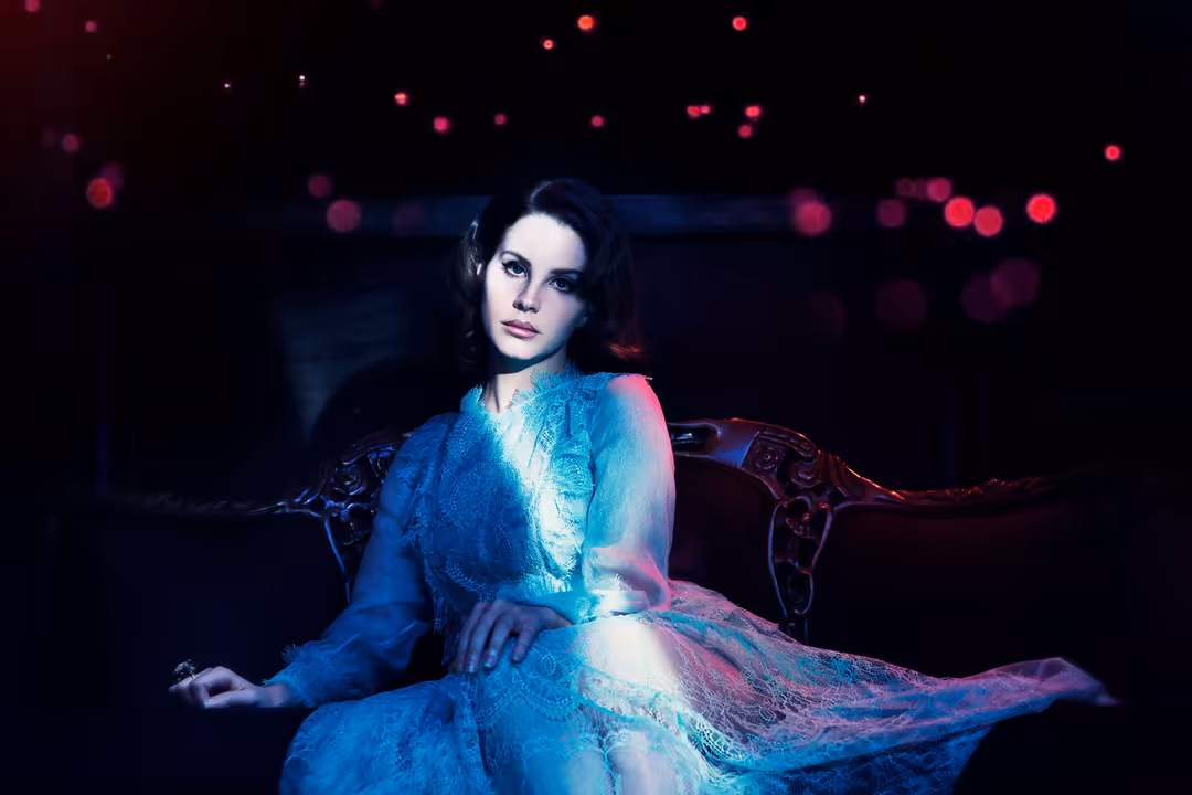 Woman in flowing blue and pink neon-lit dress seated against dark background with bokeh lights, cinematic moody aesthetic