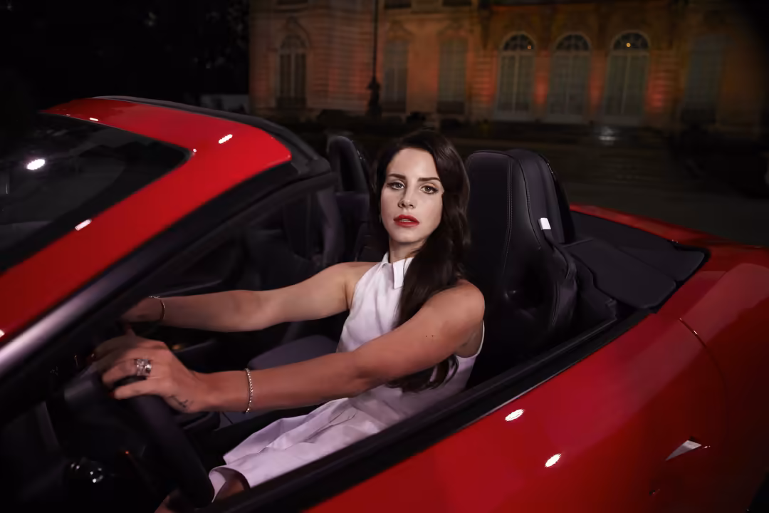 Woman in white top sitting in a red convertible car at night with illuminated historic building in background