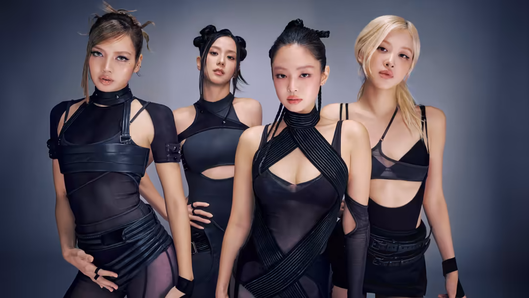 Lisa in sleek black outfit with bold makeup poses confidently with three other styled figures against a cool gray backdrop wi